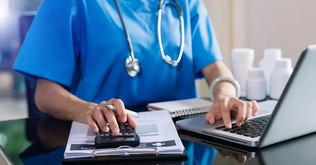 Small-practice biller working through claims with a calculator and laptop