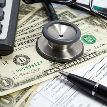 A stethoscope and pen resting on US banknotes
