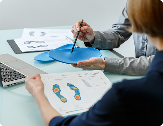 Podiatrist reviewing a custom orthotic and a foot pressure-map report with a patient