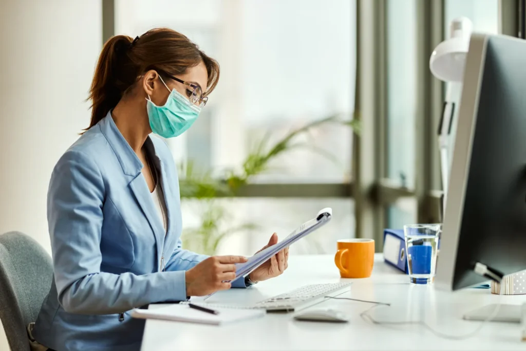 Practice administrator in a mask reviewing a claim on a tablet at her desk