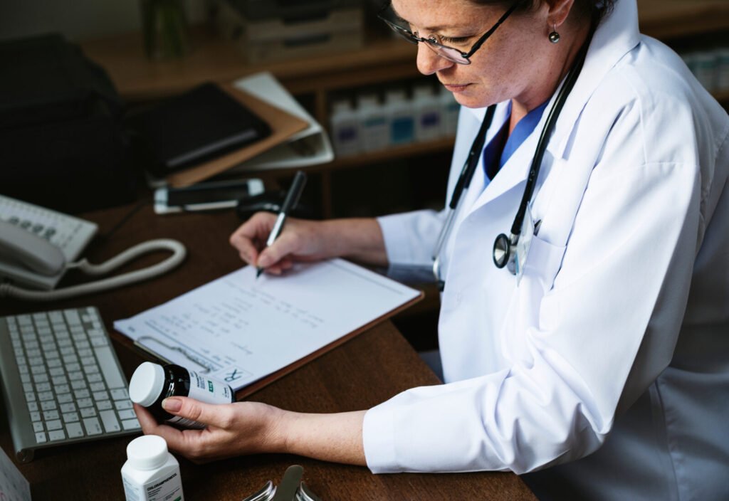 A clinician writing on a chart while holding a medication bottle at a desk