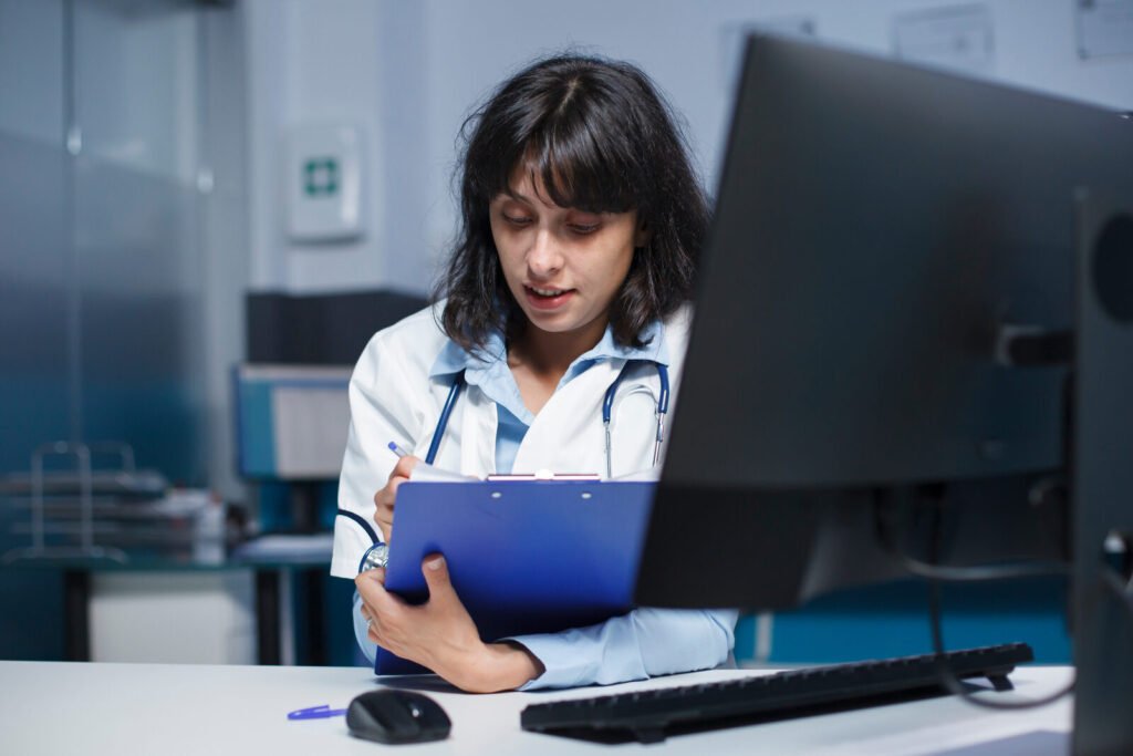 A clinician holding a clipboard while reading a monitor in a darkened office