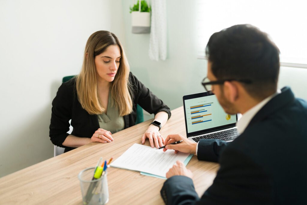 Two people reviewing enrollment paperwork and a laptop across a table