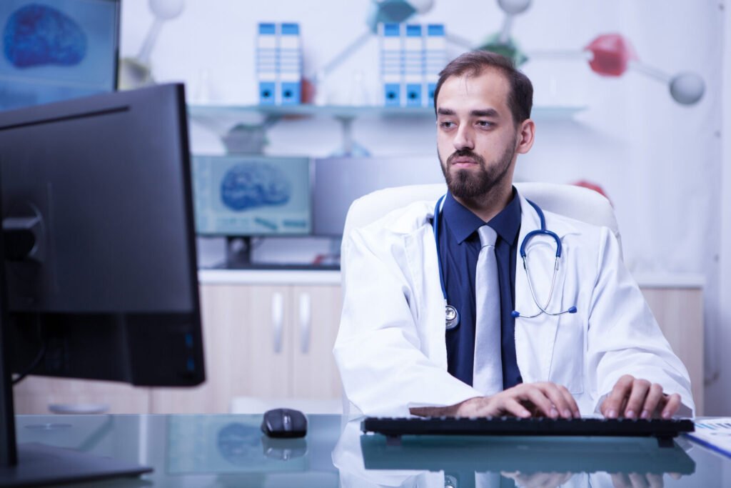 A physician typing at a dual-monitor workstation in a clinical office