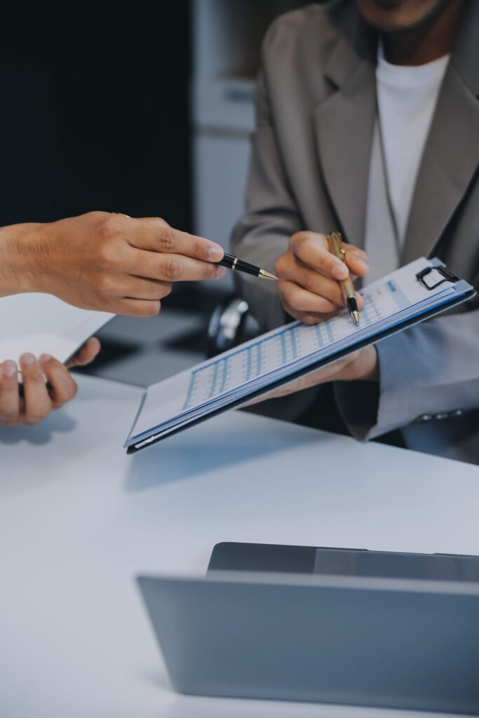 Close-up of a hand signing a form on a clipboard across a desk