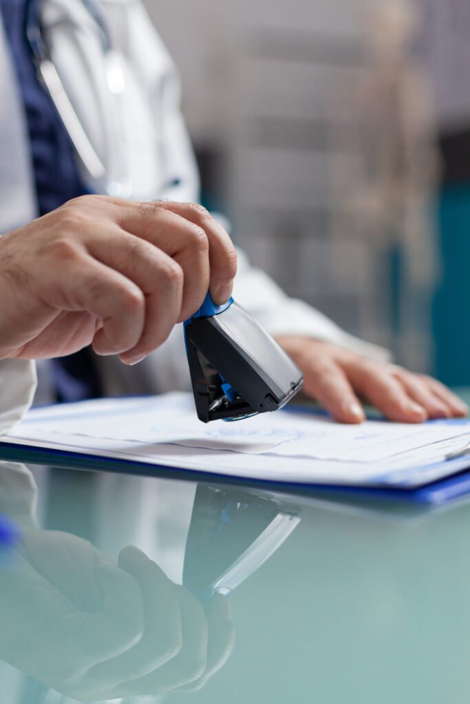 A hand signing a credentialing application on a desk