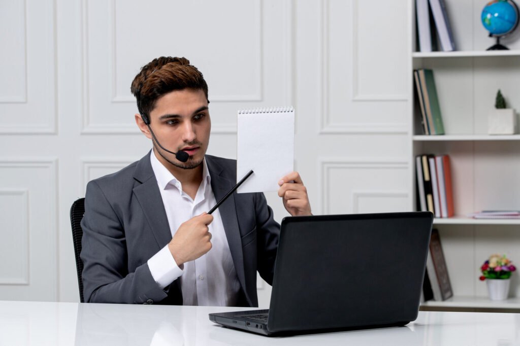A specialist wearing a headset holding a note beside a laptop