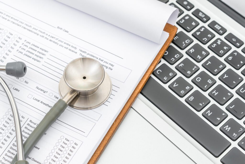A printed claim form and stethoscope resting on a laptop keyboard