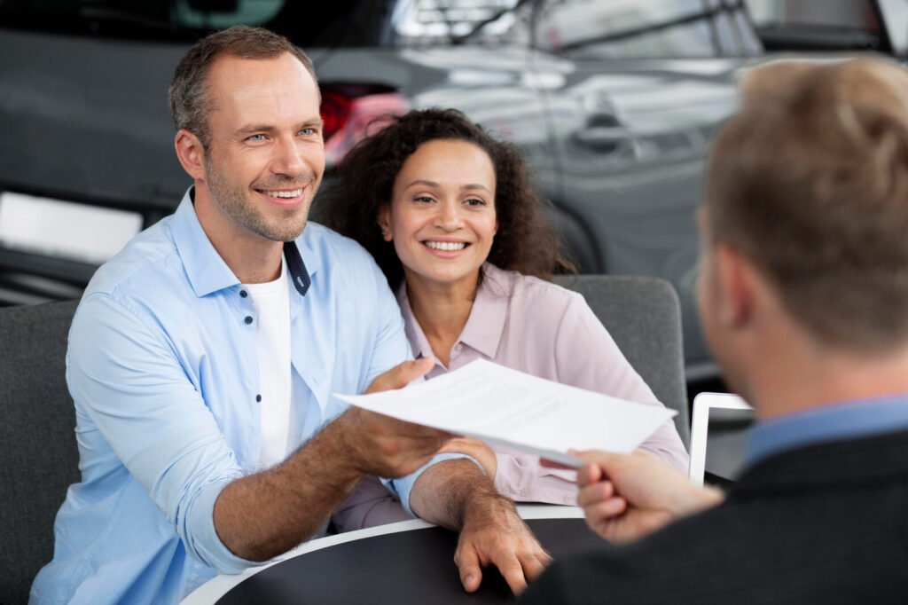 A couple passing insurance paperwork across a desk to an adviser