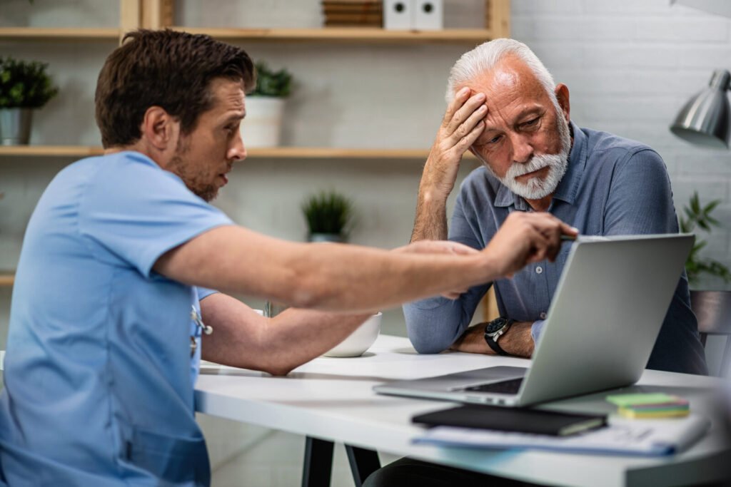 A clinician explaining a billing issue to a concerned older patient at a laptop