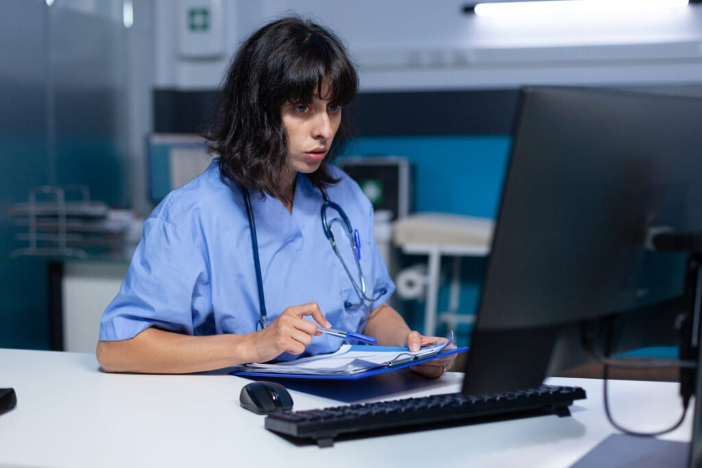 A nurse holding a clipboard while reading a monitor at a desk