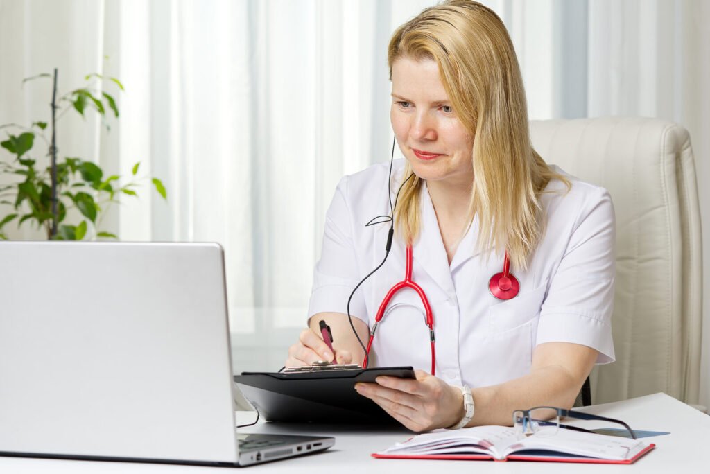 A clinician writing on a chart at a laptop in a bright office