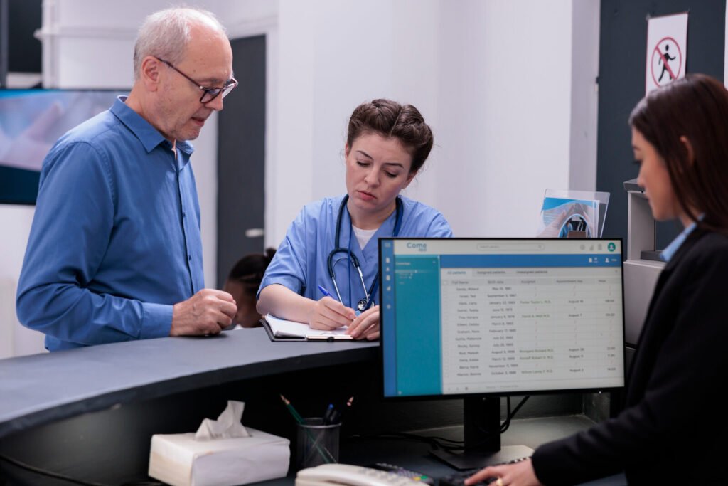 A nurse checking a patient in at a reception desk with a colleague