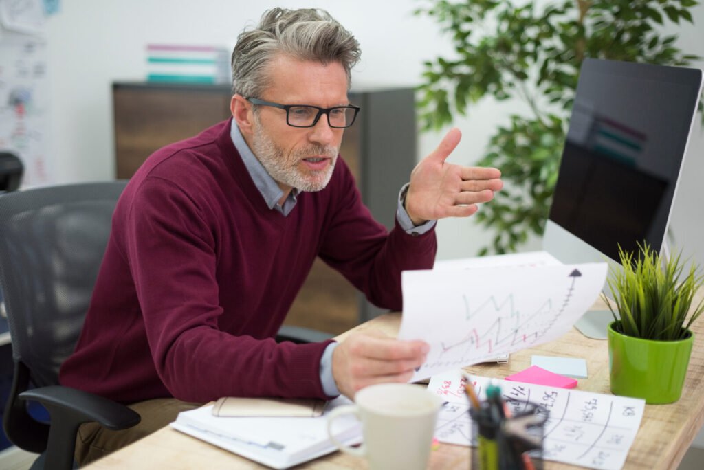 A practice manager gesturing at claim paperwork beside a monitor