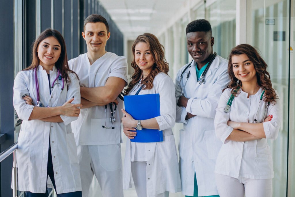 A team of five clinicians in white coats standing together in a bright hospital corridor