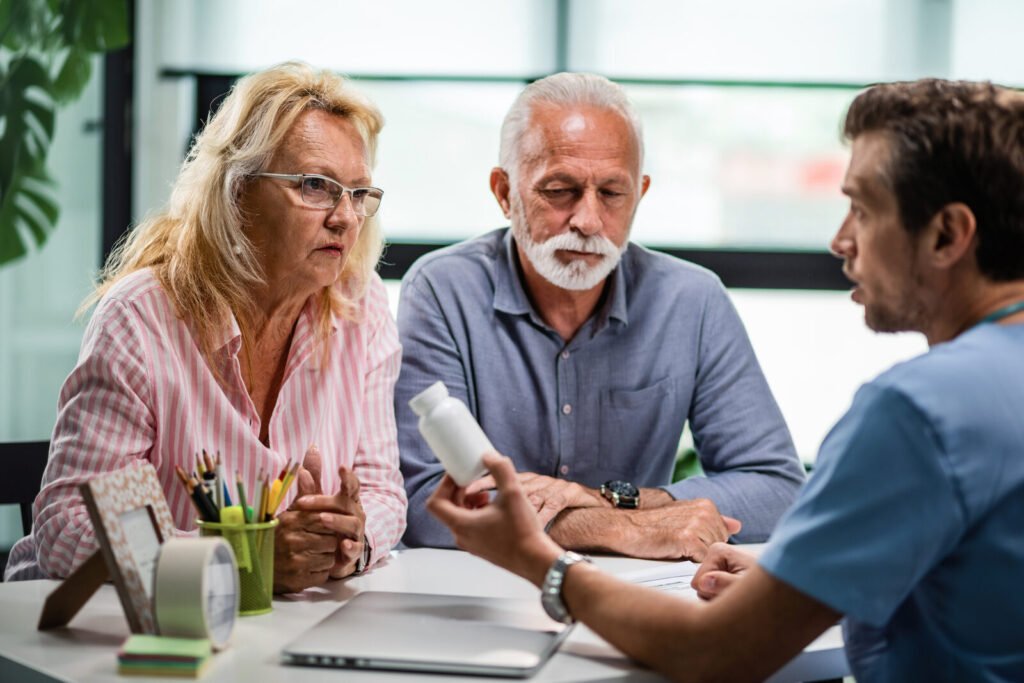 A care worker explaining a prescription to two older patients across a desk
