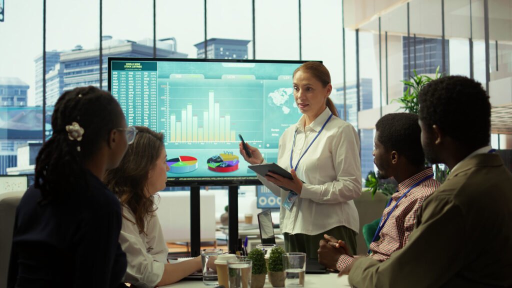 A presenter showing revenue charts on a wall screen to a seated practice team