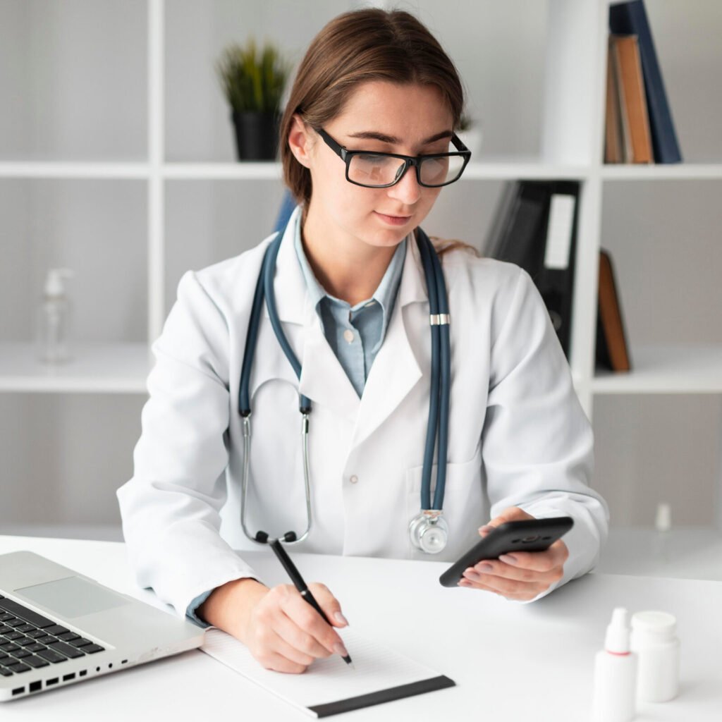 A physician writing notes at a laptop in a bright office