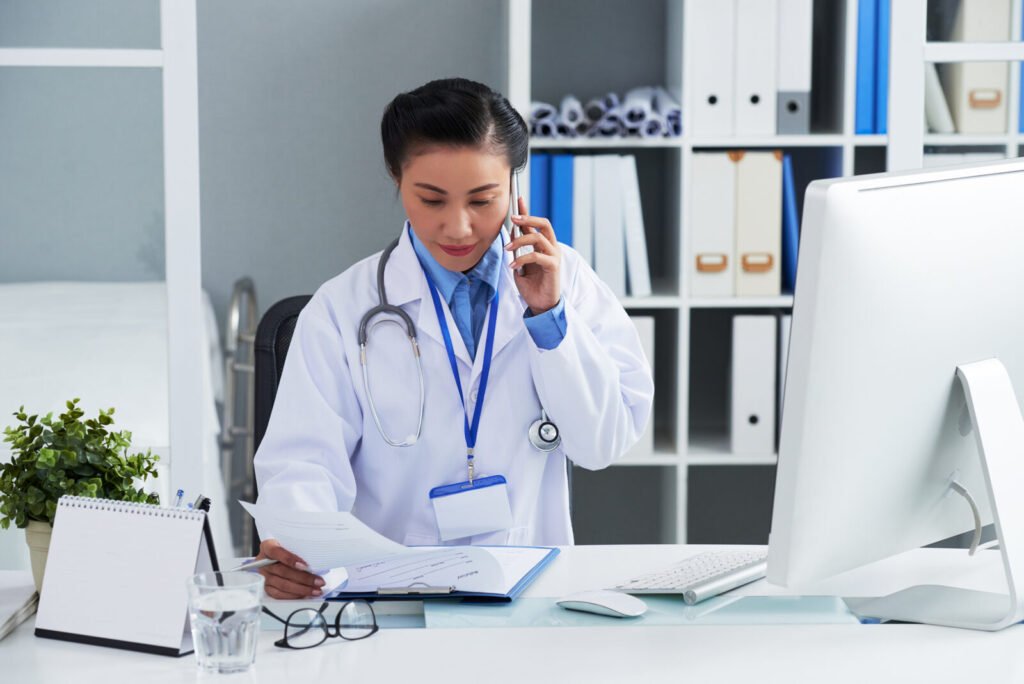 A physician on the telephone at a desk with a computer and files