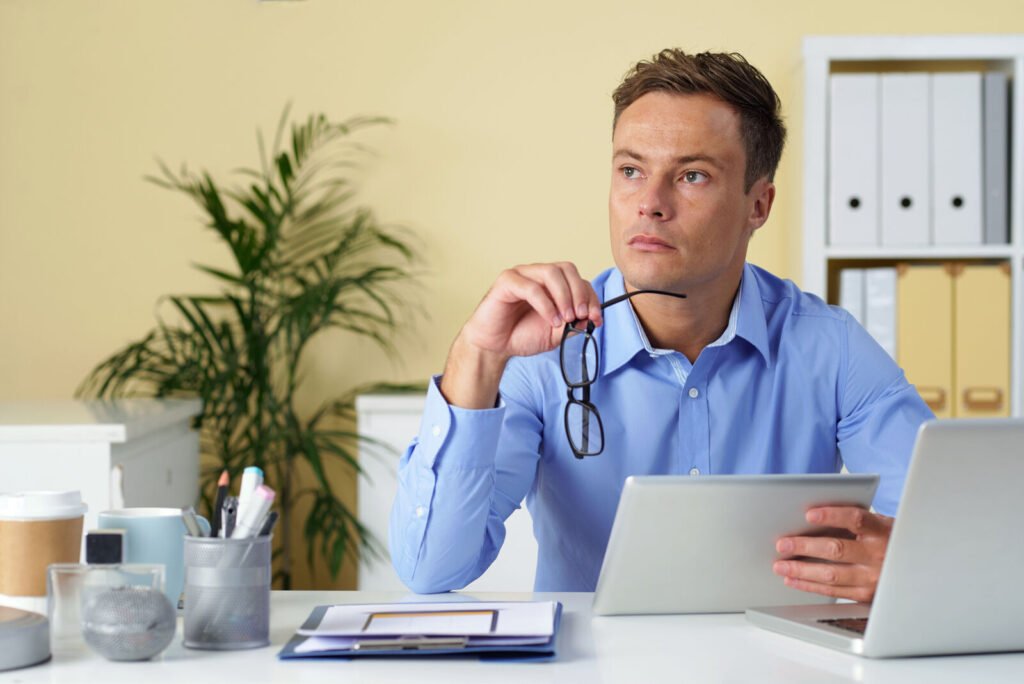 A billing specialist thinking at his desk beside a tablet