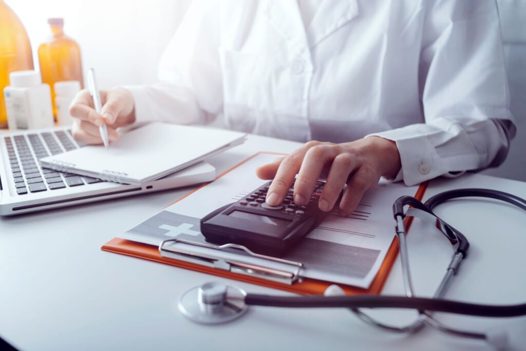 A clinician working a calculator beside claim paperwork and a stethoscope