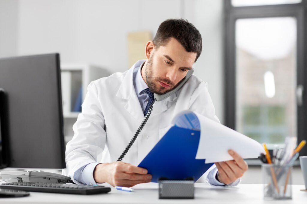 A physician on the phone holding a blue clipboard of paperwork