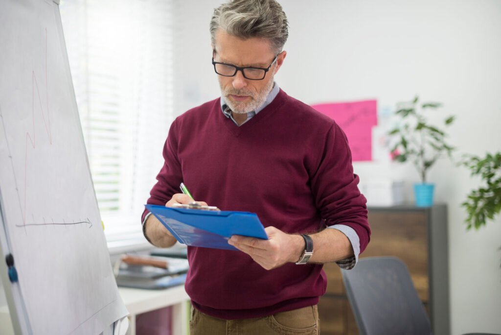 A manager in glasses reviewing trip records on a blue clipboard