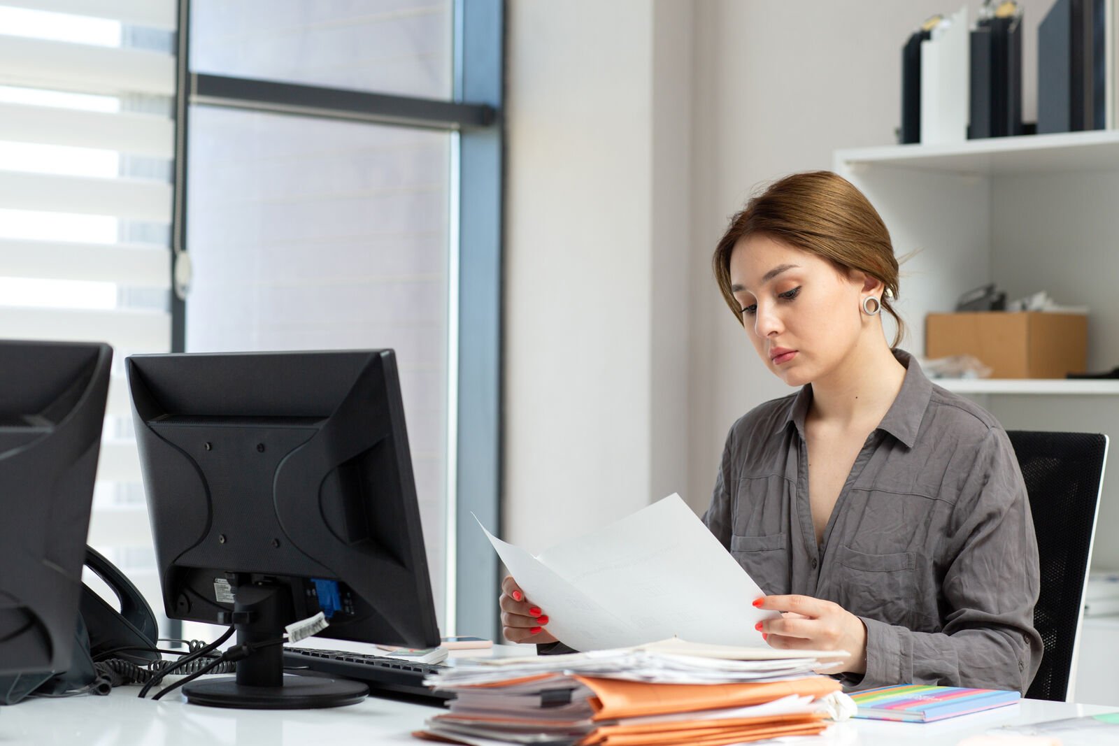 A billing specialist reviewing printed trip logs at a desk with two monitors