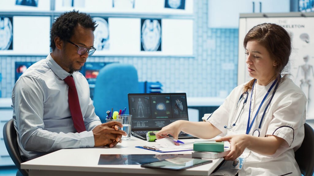 A physician and a colleague reviewing paperwork together at a desk beside a laptop