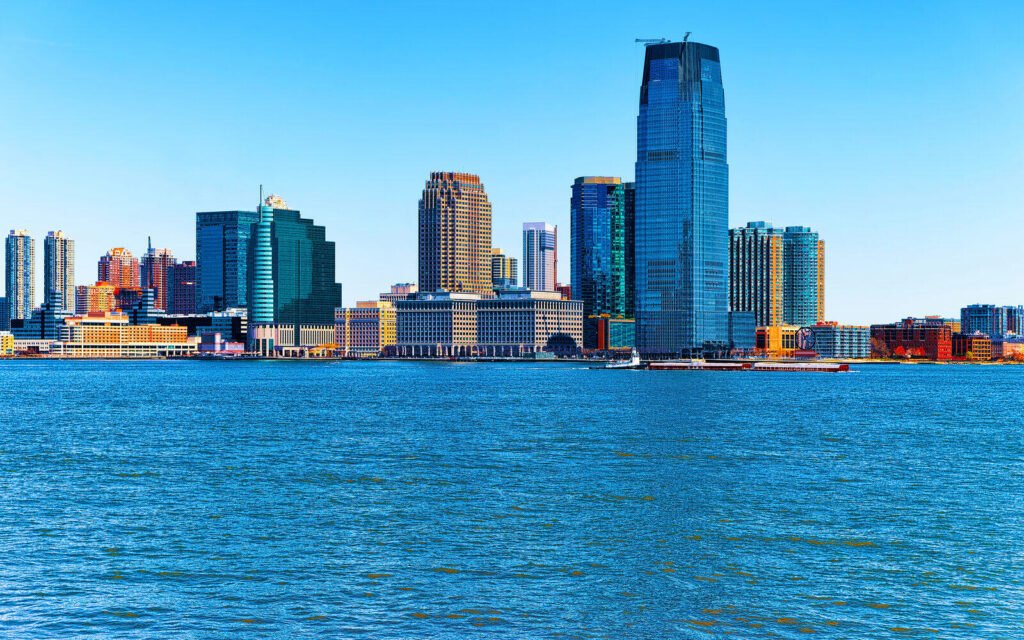 The Jersey City skyline on the Hudson River waterfront under a clear blue sky