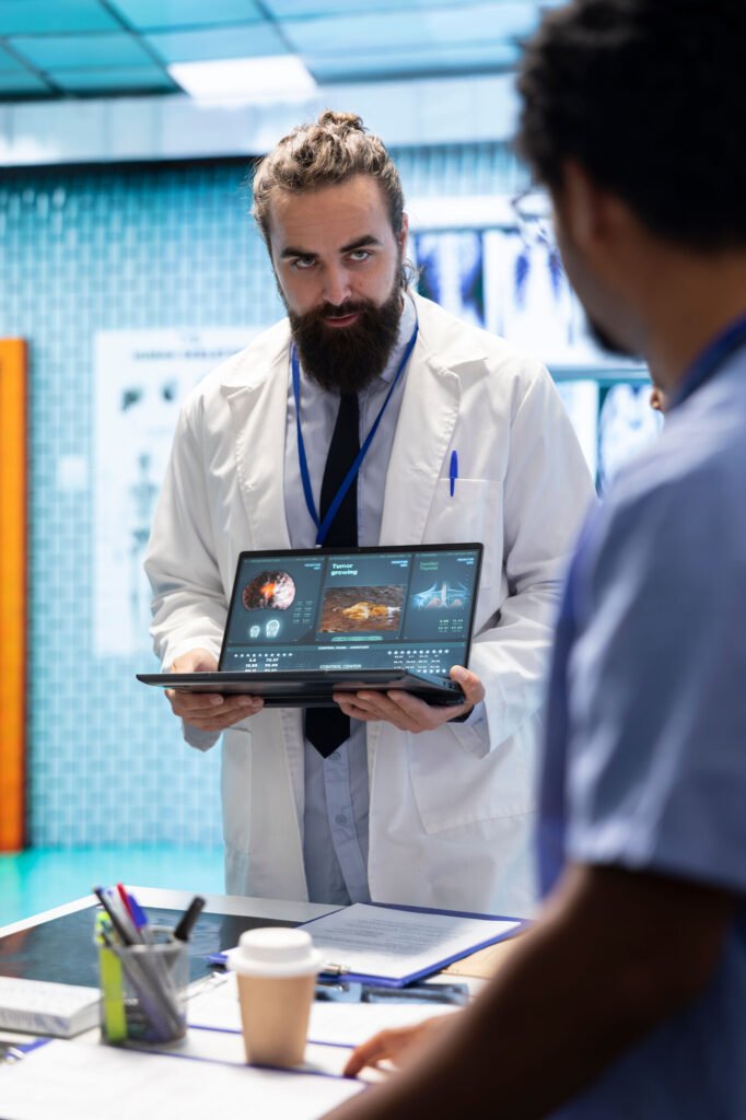 A physician holding up a laptop to show a colleague