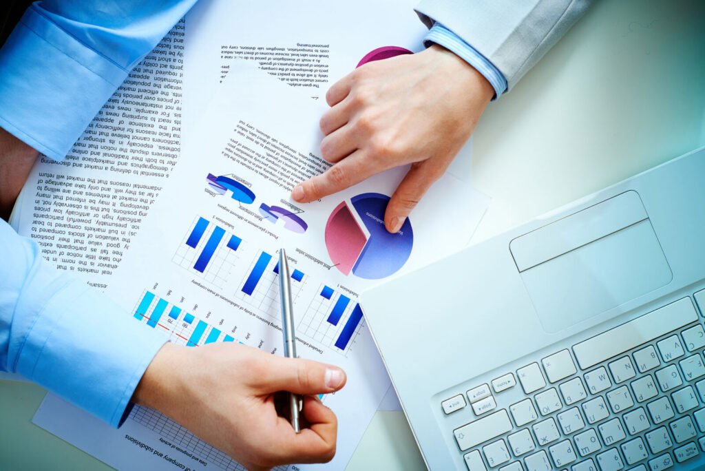 Hands pointing at revenue charts on a printed report beside a laptop