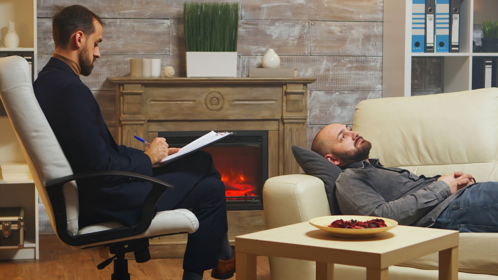 A psychiatrist taking notes during a session with a patient resting on a couch