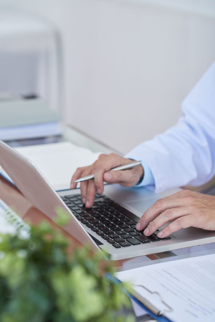 Hands typing on a laptop beside paperwork
